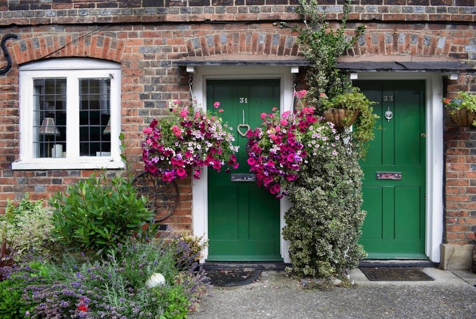 A close-up view of two small, green front doors numbered 31 and 33, set into a red brick wall of a residential building. The doors are framed by white trim and feature letterboxes, door knockers, and 